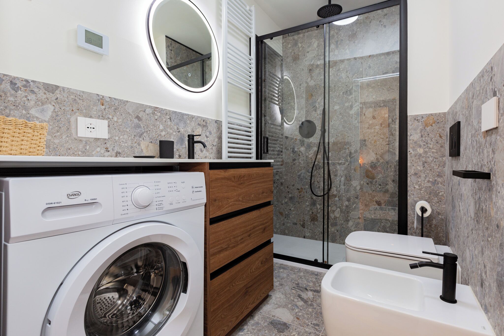 Un bagno moderno con lavatrice integrata, cabina doccia in vetro e lavandino bianco.