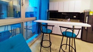 A modern kitchen with a white countertop, two bar stools, and a window with blue curtains. - a una cuadra de la playa  (Santa Marta)