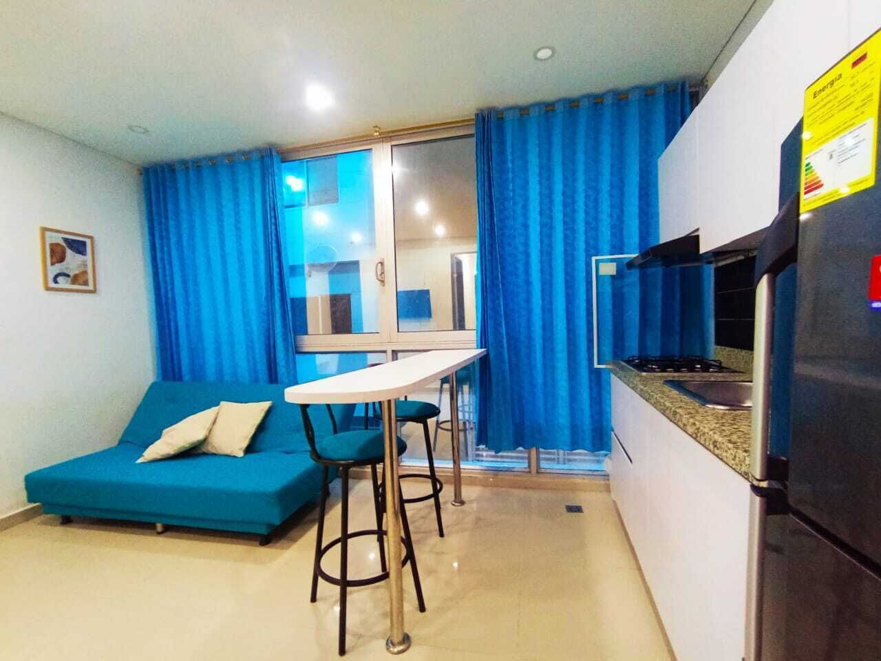A compact living space with a kitchenette, a blue sofa, a small dining table, and a glass door leading to a balcony.