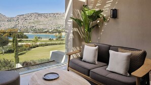 A balcony with a sofa, a table, and a view of a lake and hills. - Amoh, A Luxury Collection Resort, Rhodes (Rhodes)