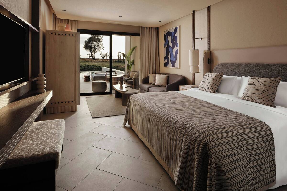 A hotel room with a large bed, a TV, a sofa, a desk, and a view of the outdoors.