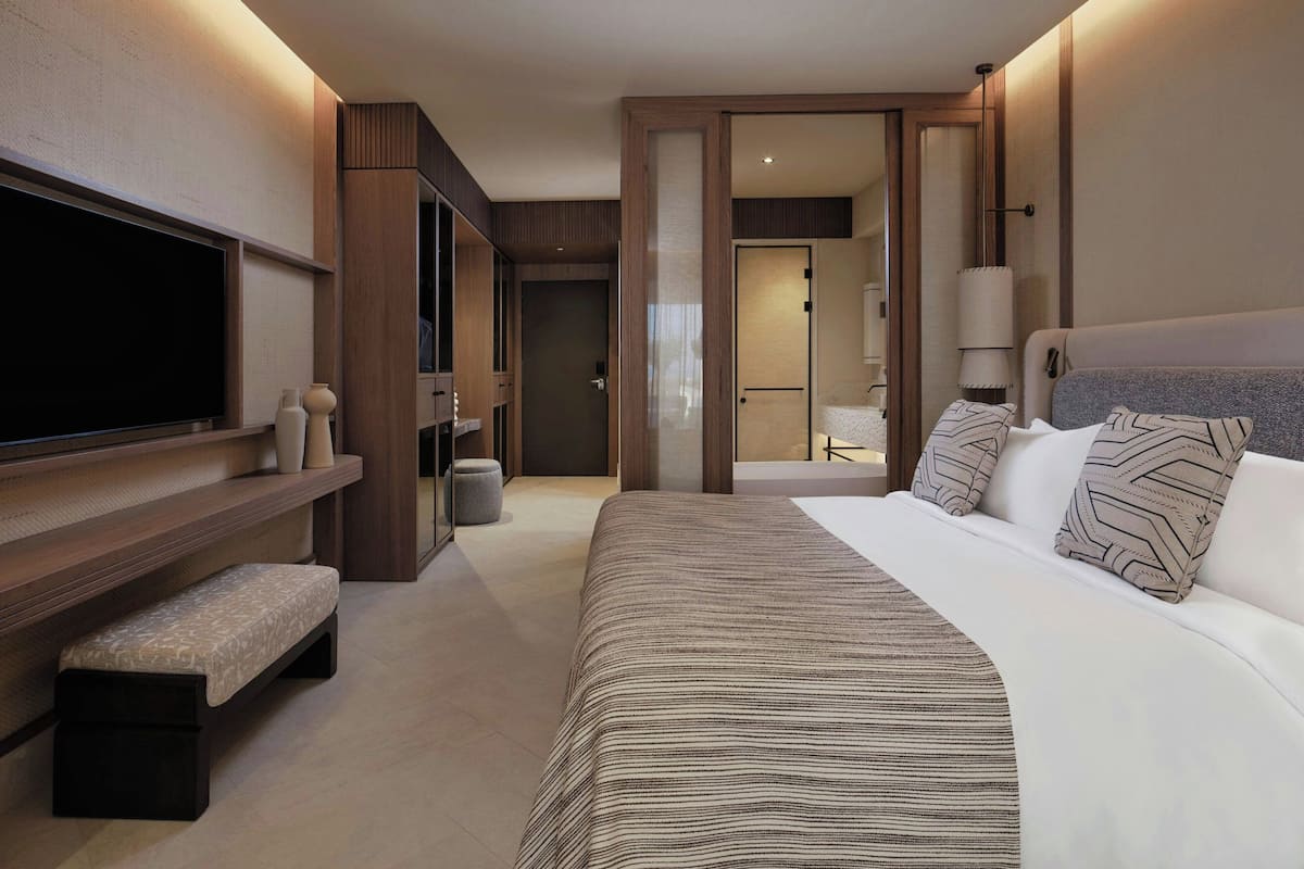 A modern hotel room with a large bed, a TV, a bench, and a walk-in closet.
