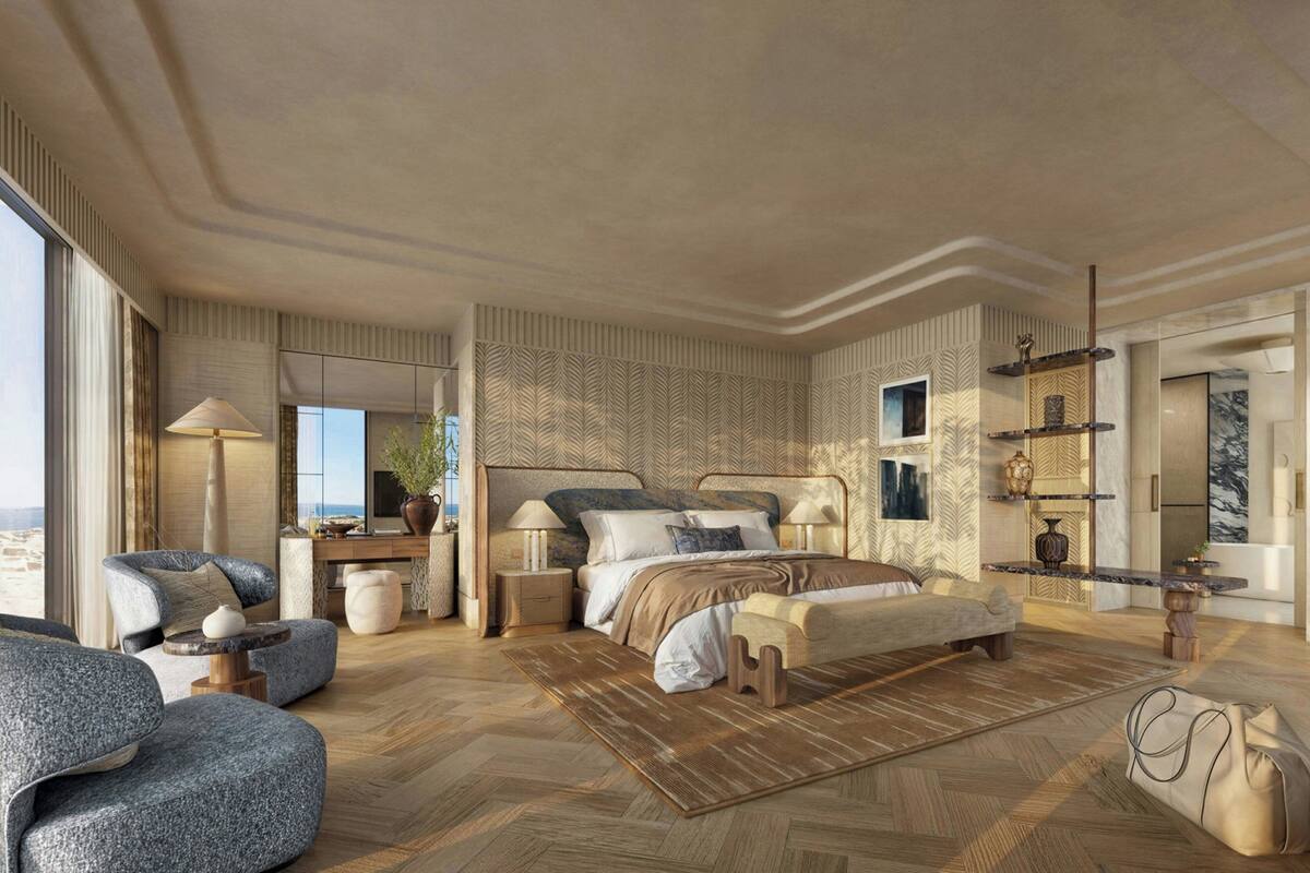 A spacious bedroom with a large bed, a sitting area with a sofa and armchair, a desk, and a view of the outdoors.