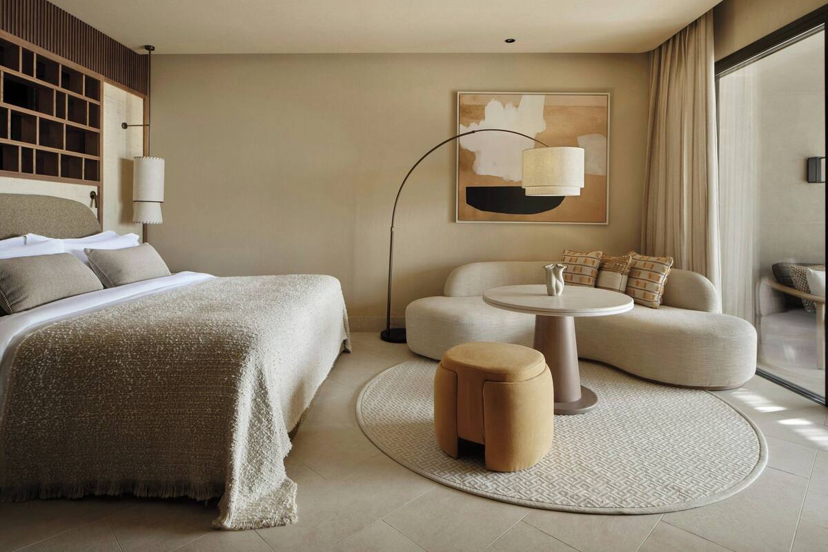 A hotel room with a bed, a sofa, a round table, and a lamp.