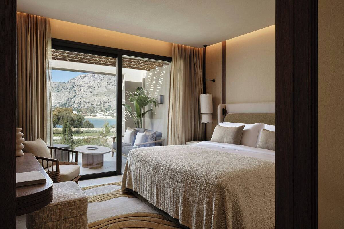 A hotel room with a bed, a seating area, a small table, and a view of a mountainous landscape.