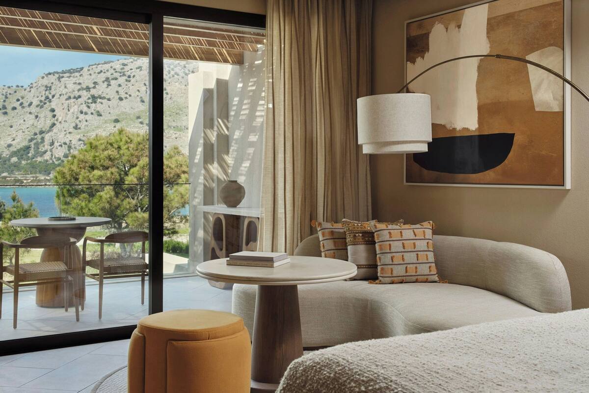 A modern hotel room with a balcony, a round table, a sofa, and a painting.