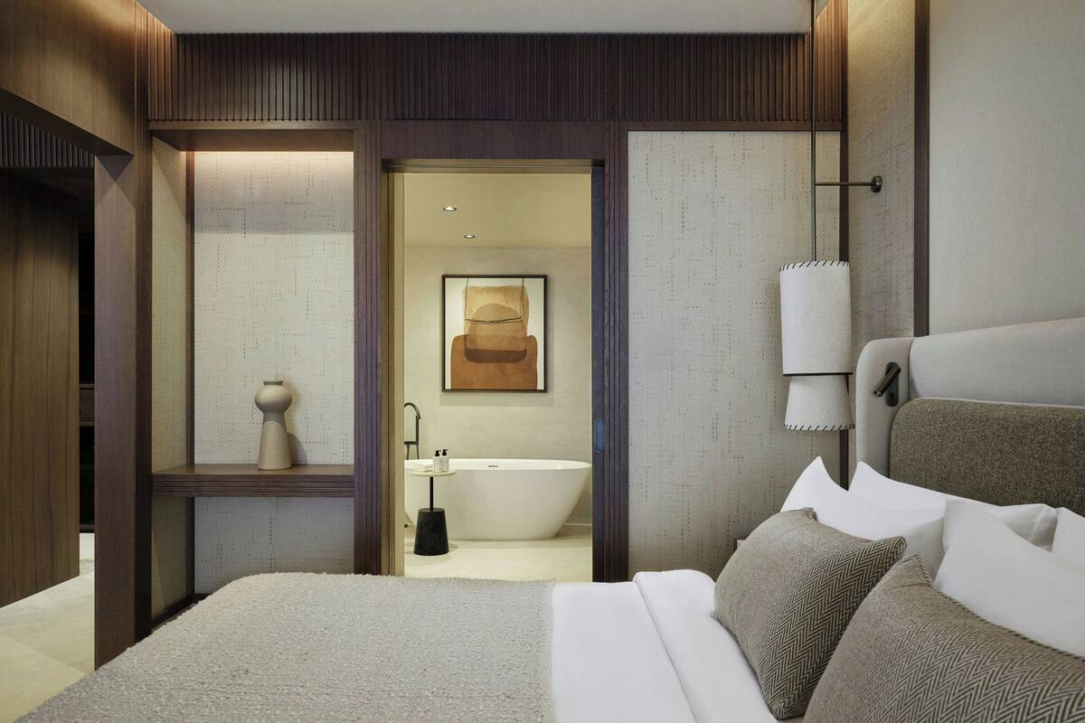 A modern hotel room with a large bed, a bathtub, and a small sitting area with a chair and table.