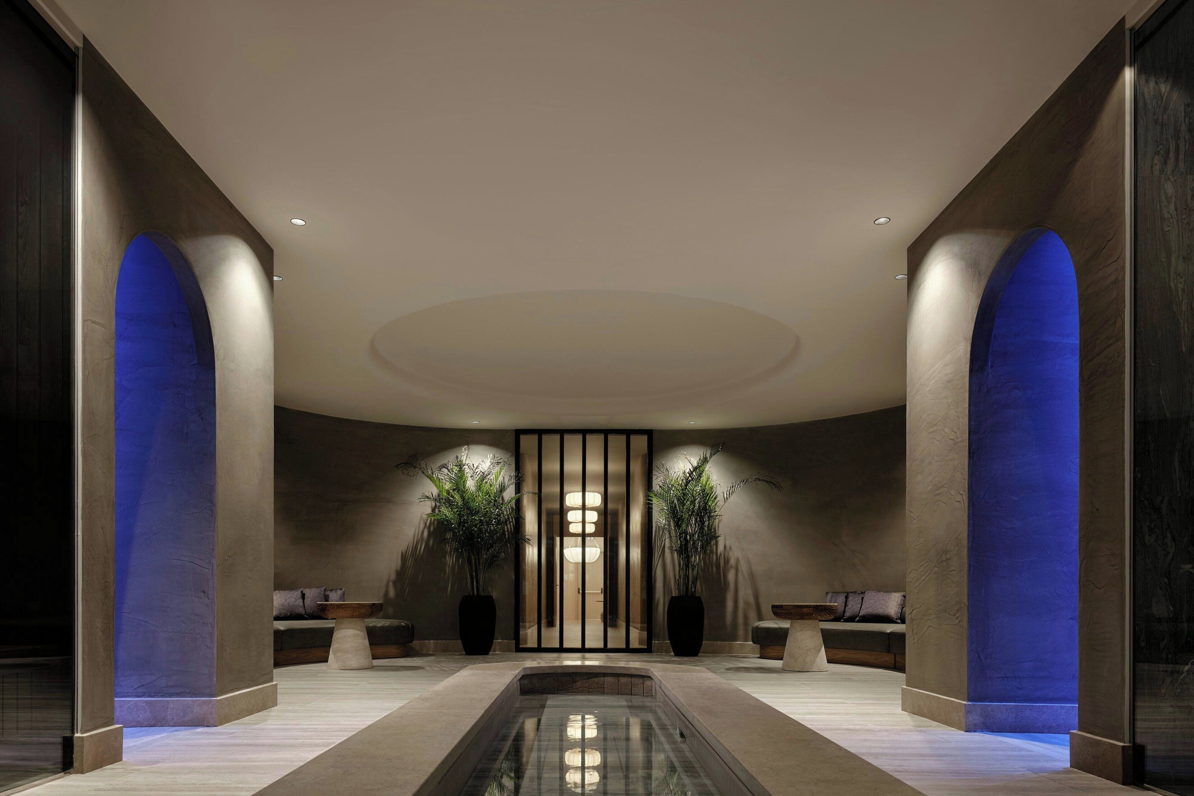 A modern lobby with a central water feature, seating areas, and tall columns.