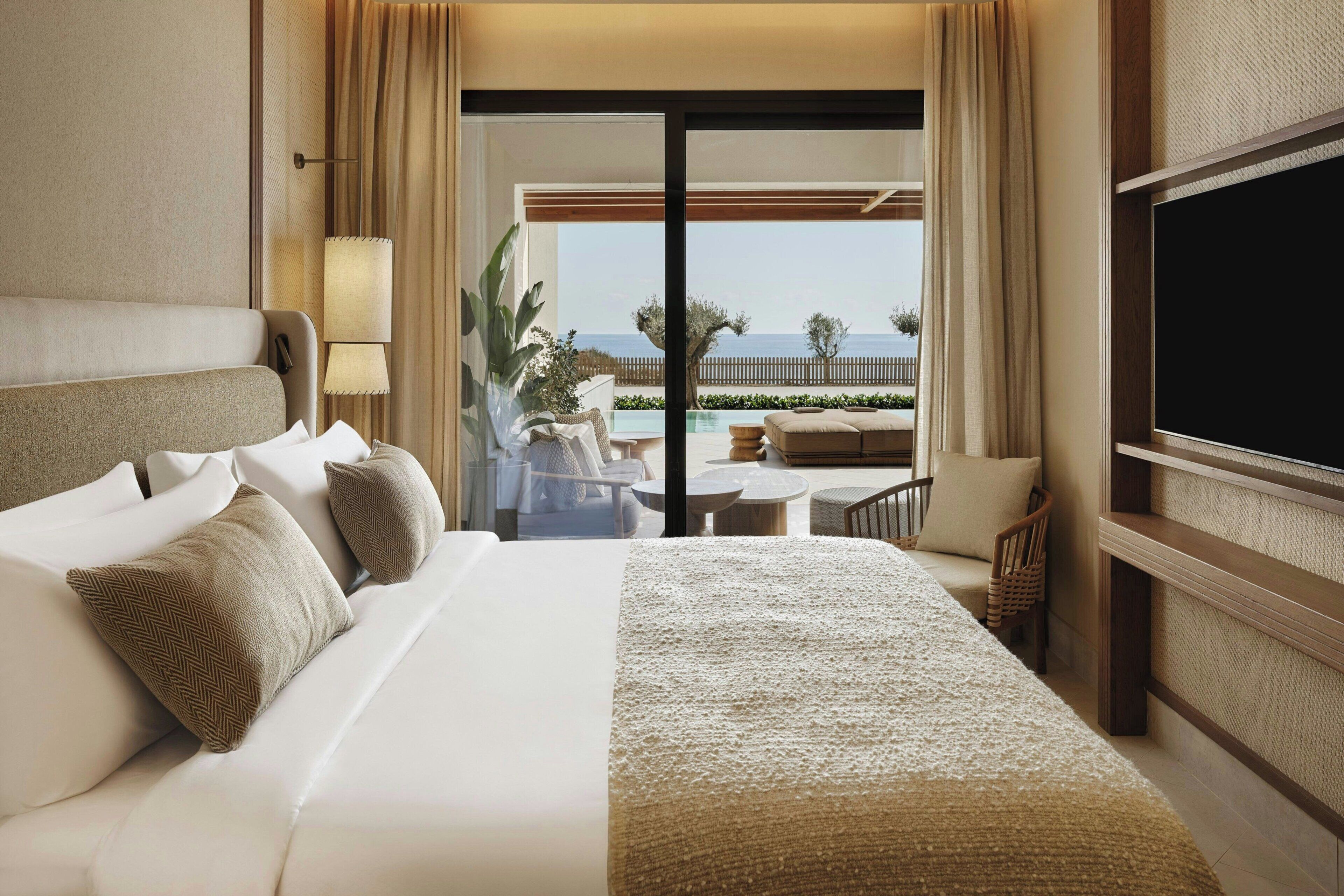 A hotel room with a bed, a TV, a balcony with a view of the sea, and a dining area.