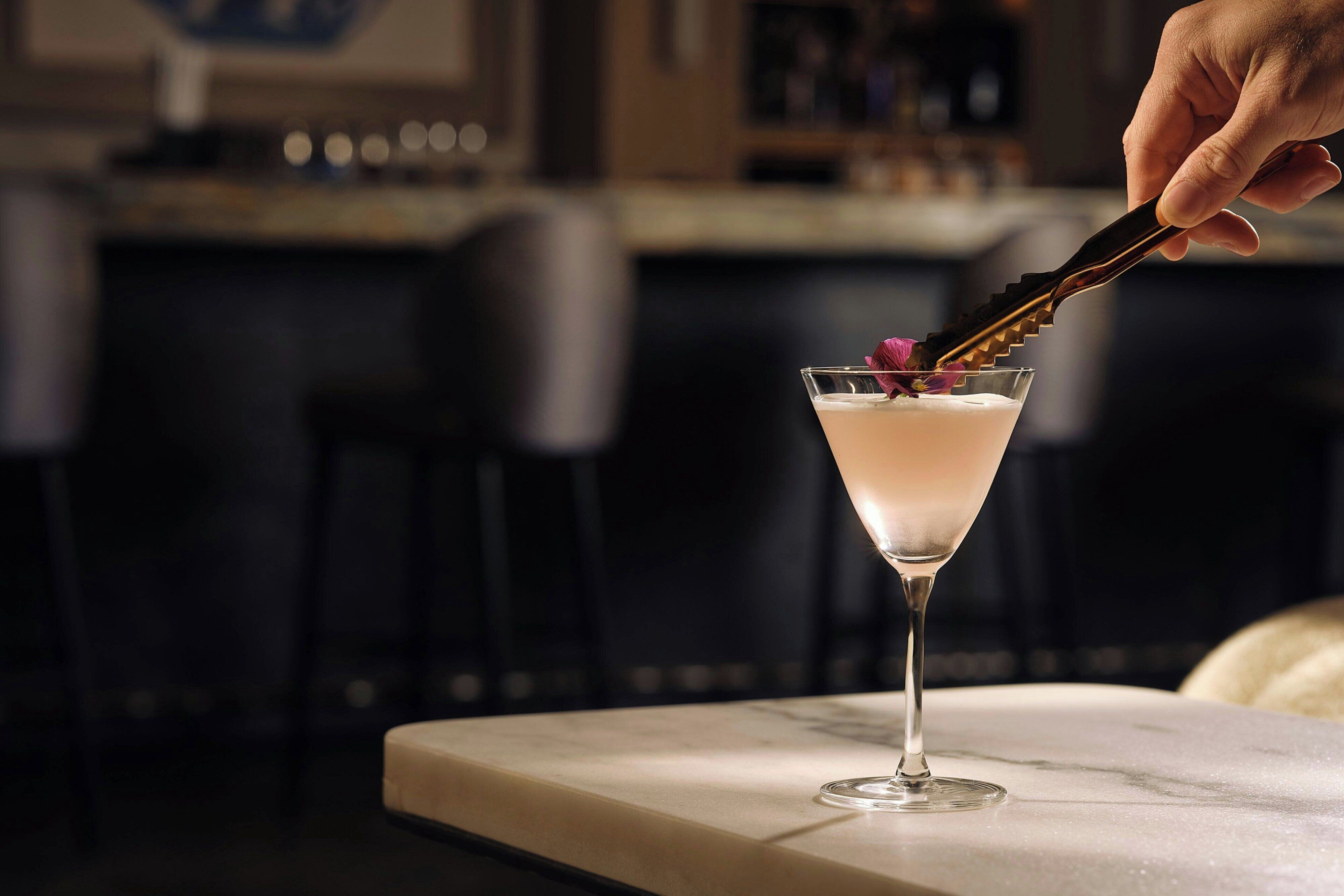 A martini glass with a flower garnish on a marble bar counter.
