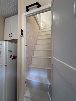 En trappa som leder upp till andra våningen, med ett vitt räcke och en dörr med ett svart handtag.