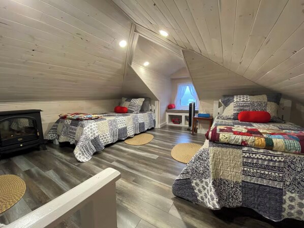 Ein gemütliches Schlafzimmer im Dachgeschoss mit zwei Betten, Holzboden und einem alten Kochherd.
