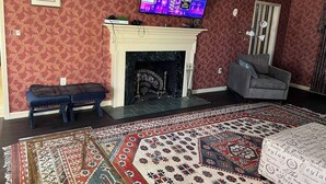 A living room with a fireplace, a television, a bench, and a patterned rug. - Spacious 7-bedroom house on quiet cul-de-sac in heart of Plattsburgh (Plattsburgh)