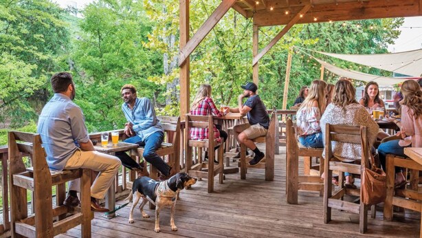 An outdoor wooden deck with tables and chairs, surrounded by greenery.