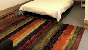 A bedroom with a bed, a colorful striped rug, a white wall, and a blue painting.