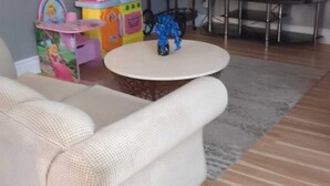 A living room with a white sofa, a round coffee table, a TV, and a small play area with toys. - Whole House: Fair Price Great Amenities (Richmond Hill)