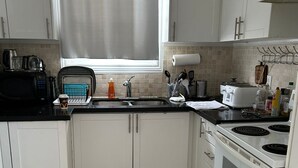 A kitchen with white cabinets, a black countertop, a white stove, and a window with a curtain. - Whole House: Fair Price Great Amenities (Richmond Hill)