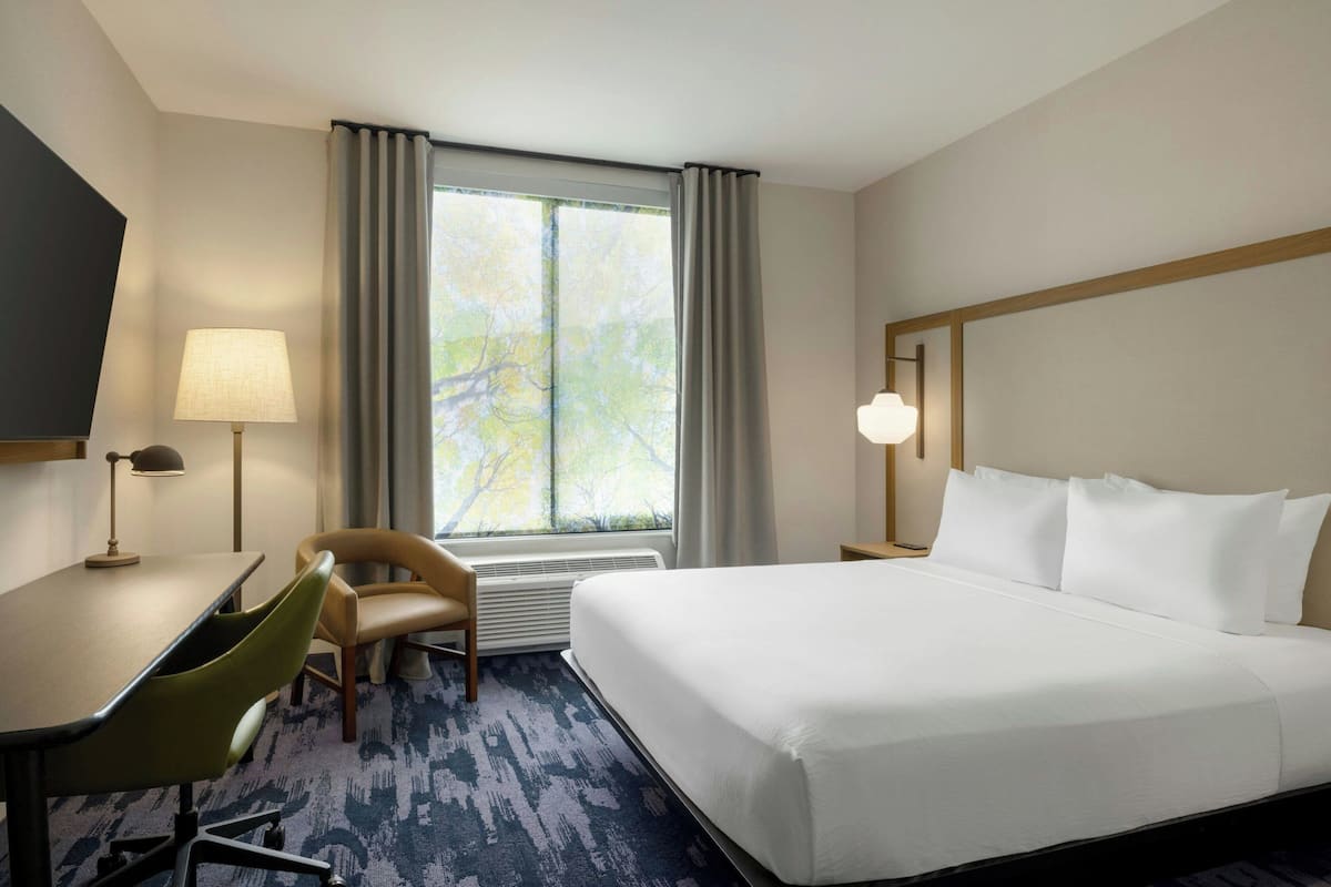 A hotel room with a large bed, a desk with a chair, a TV, and a window with curtains.