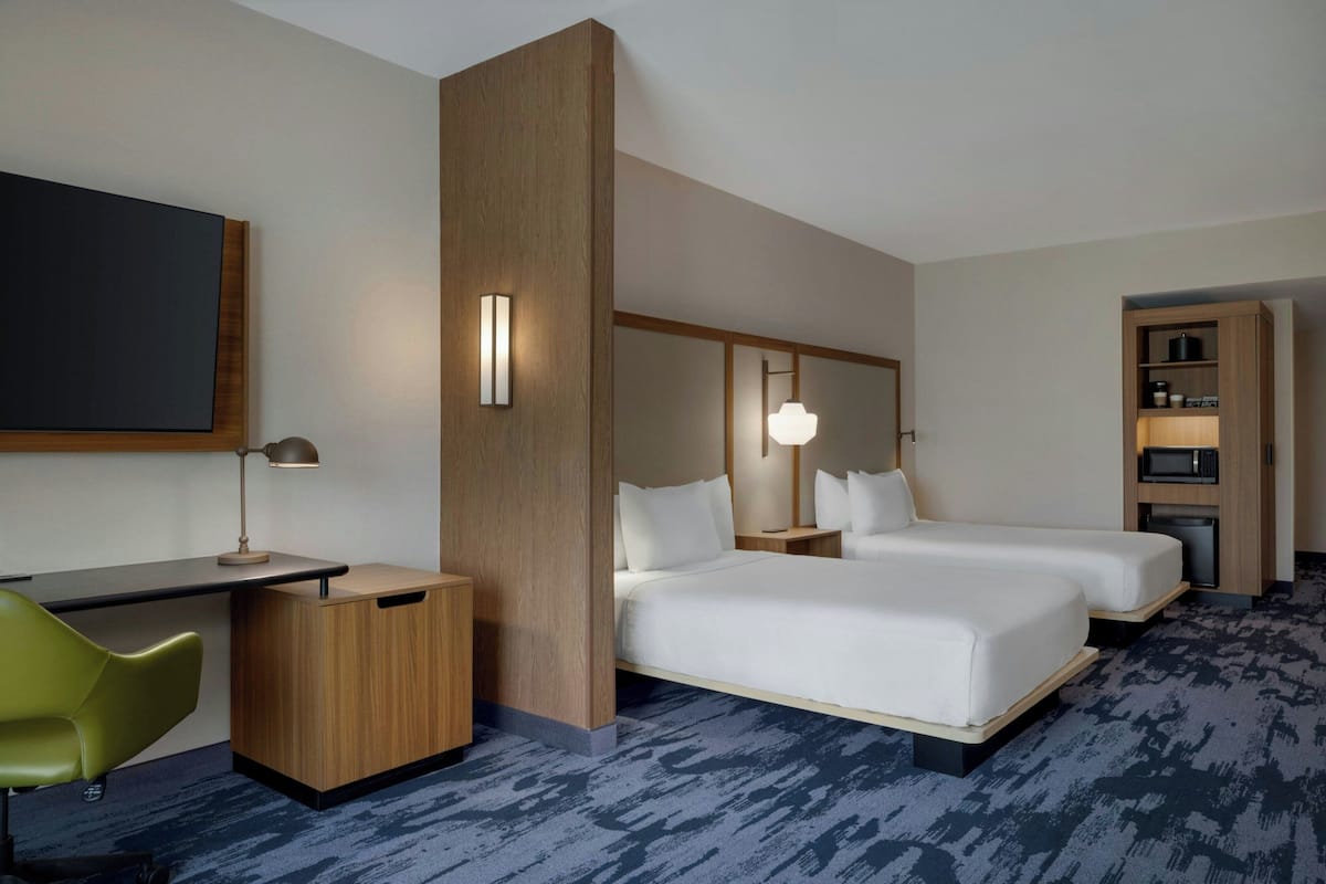 A hotel room with a desk, two beds, a chair, a wardrobe, and a built-in microwave.