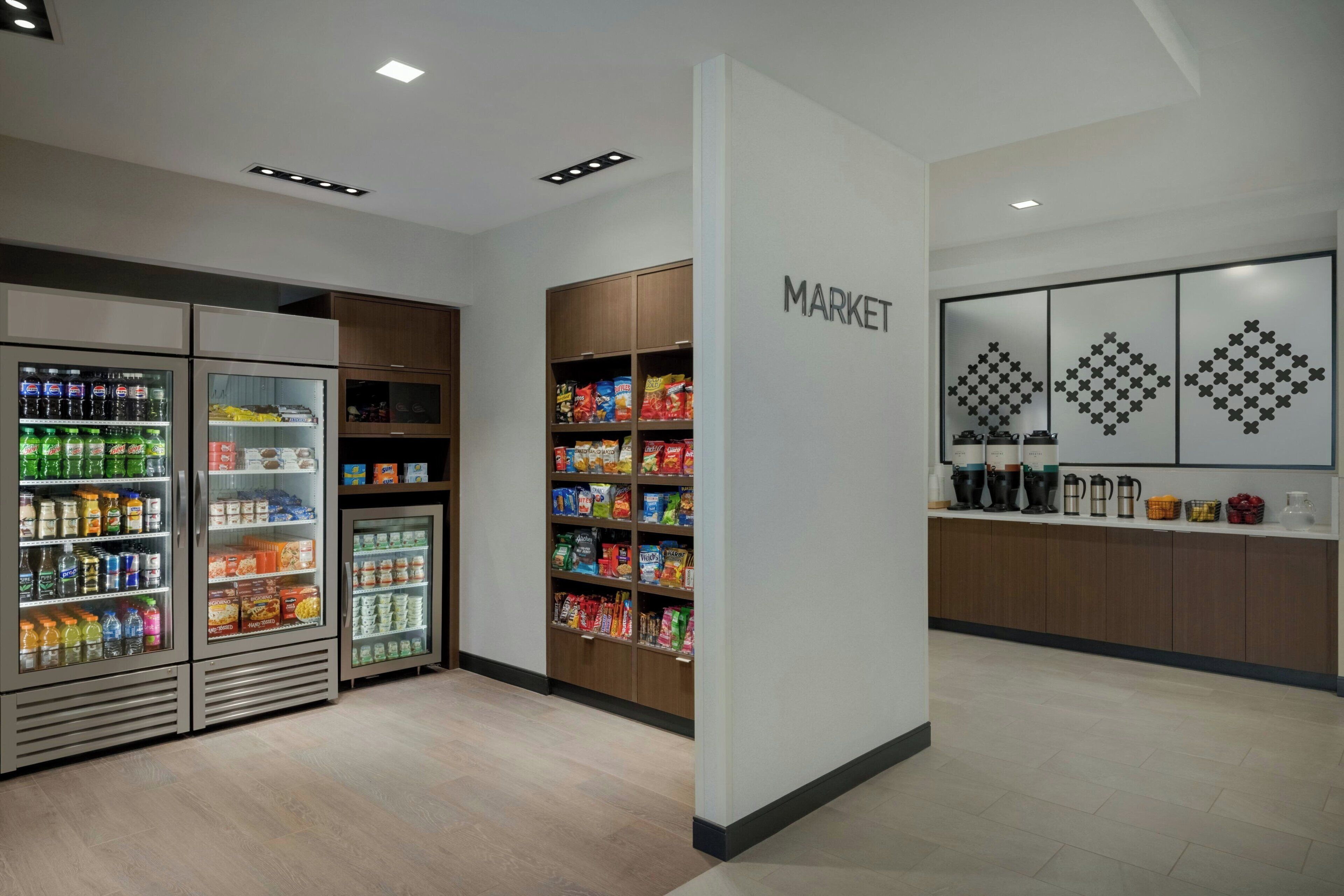 A clean, well-lit store with refrigerated beverage coolers, snack shelves, and a coffee station.