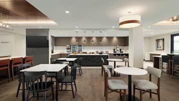 Un interno ristorante moderno con un'area bar centrale, diverse opzioni di posti a sedere e una lavagna con il menu ben visibile.
