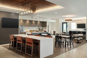 Una cocina moderna con una isla central, iluminación colgante y un televisor de pantalla plana grande.