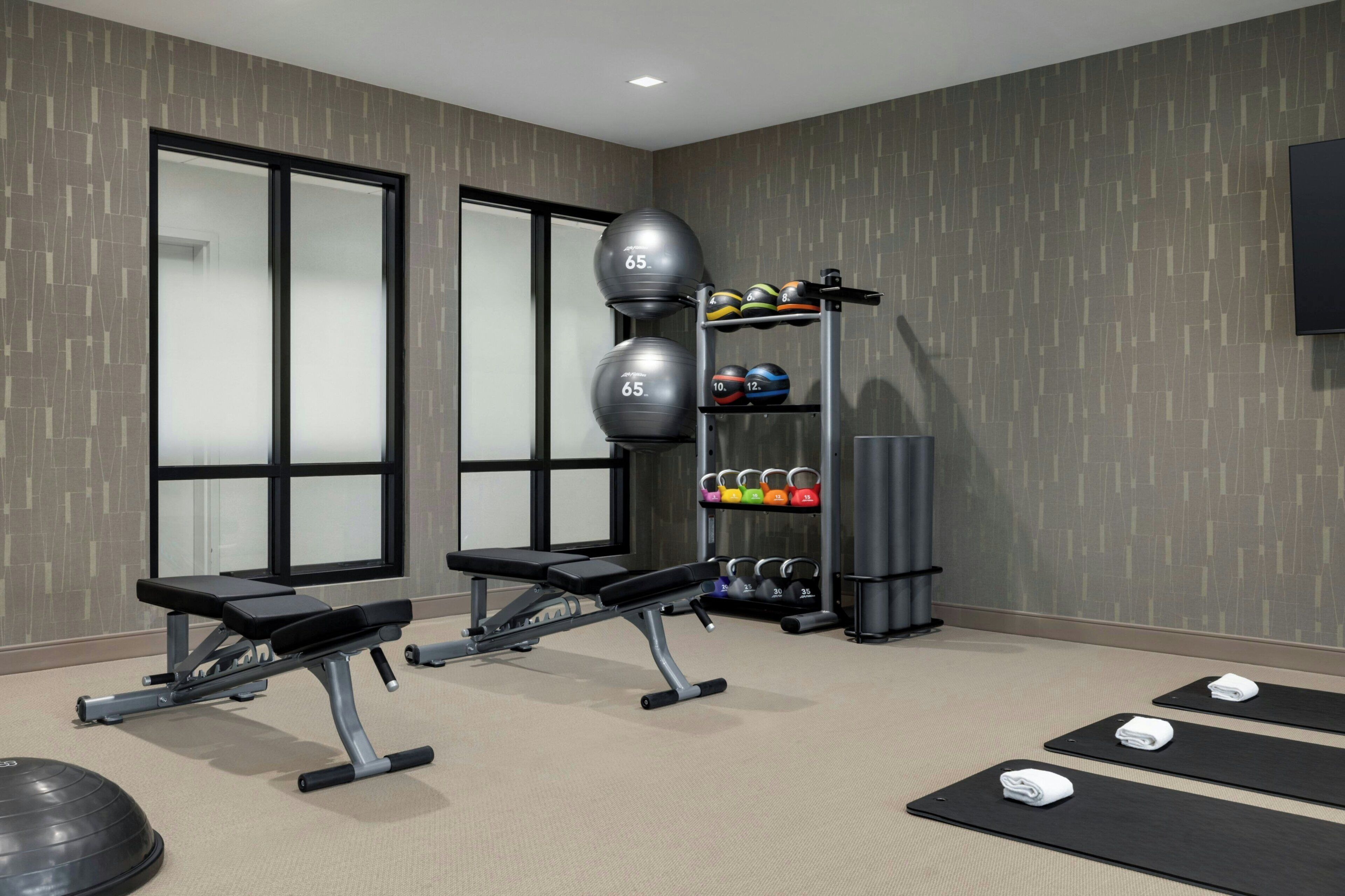 A gym with exercise equipment, weightlifting benches, and a rack of dumbbells.