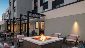 A modern outdoor seating area with a fire pit, lounge chairs, and tables, surrounded by a building with large windows and a covered walkway. - Towneplace Suites By Marriott Lancaster, PA (Lancaster)