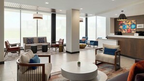 A modern hotel lobby with a reception desk, seating area with sofas and chairs, large windows, and a decorative wall piece. - Towneplace Suites By Marriott Lancaster, PA (Lancaster)