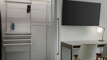 A modern room with a desk, two chairs, a TV mounted on the wall, and a shelving unit with various items.