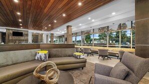 A modern lounge area with a wooden ceiling, comfortable seating, a large TV screen, and large windows offering views of the outside.