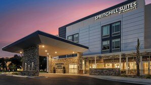 A modern hotel entrance with a stone facade, large windows, and a covered parking area.