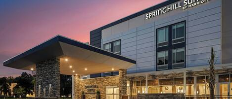 A modern hotel entrance with a stone facade, large windows, and a covered parking area.