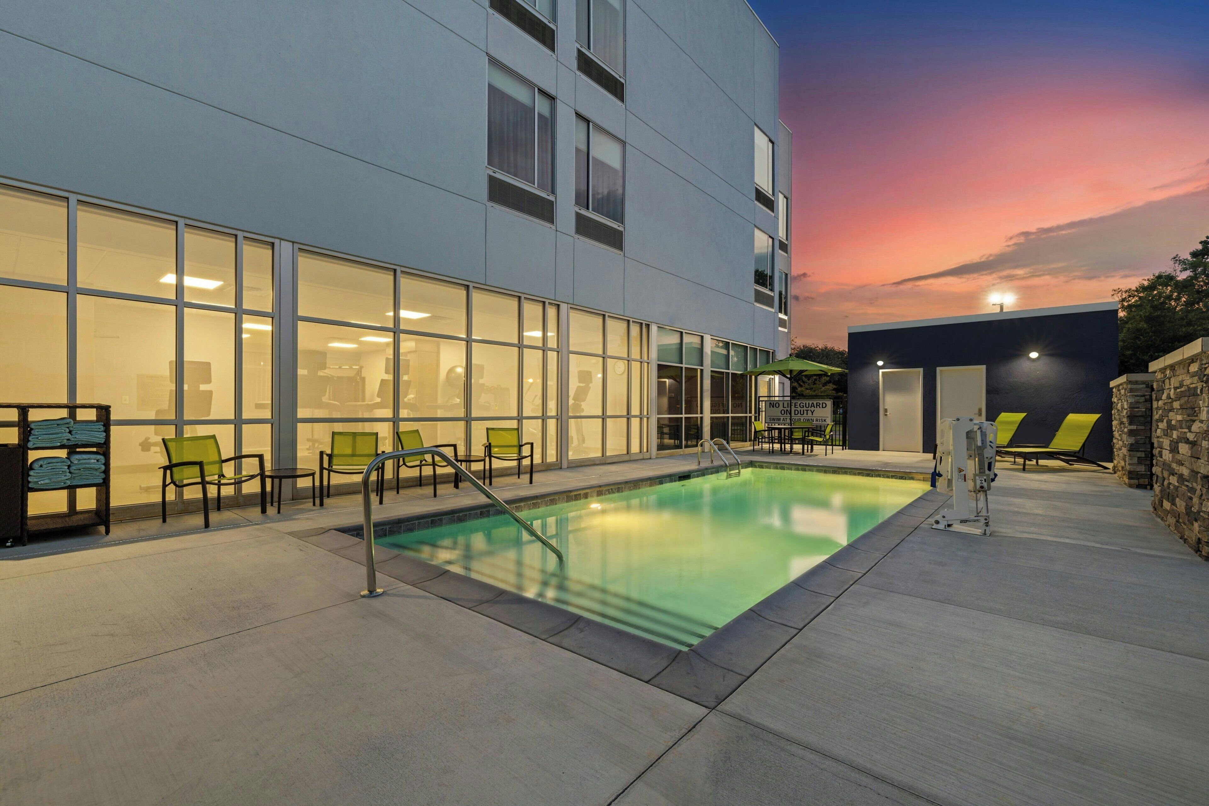 Un edificio moderno con piscina, mobiliario exterior y un cielo al atardecer.
