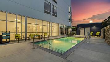 Un edificio moderno con piscina, mobiliario exterior y un cielo al atardecer.