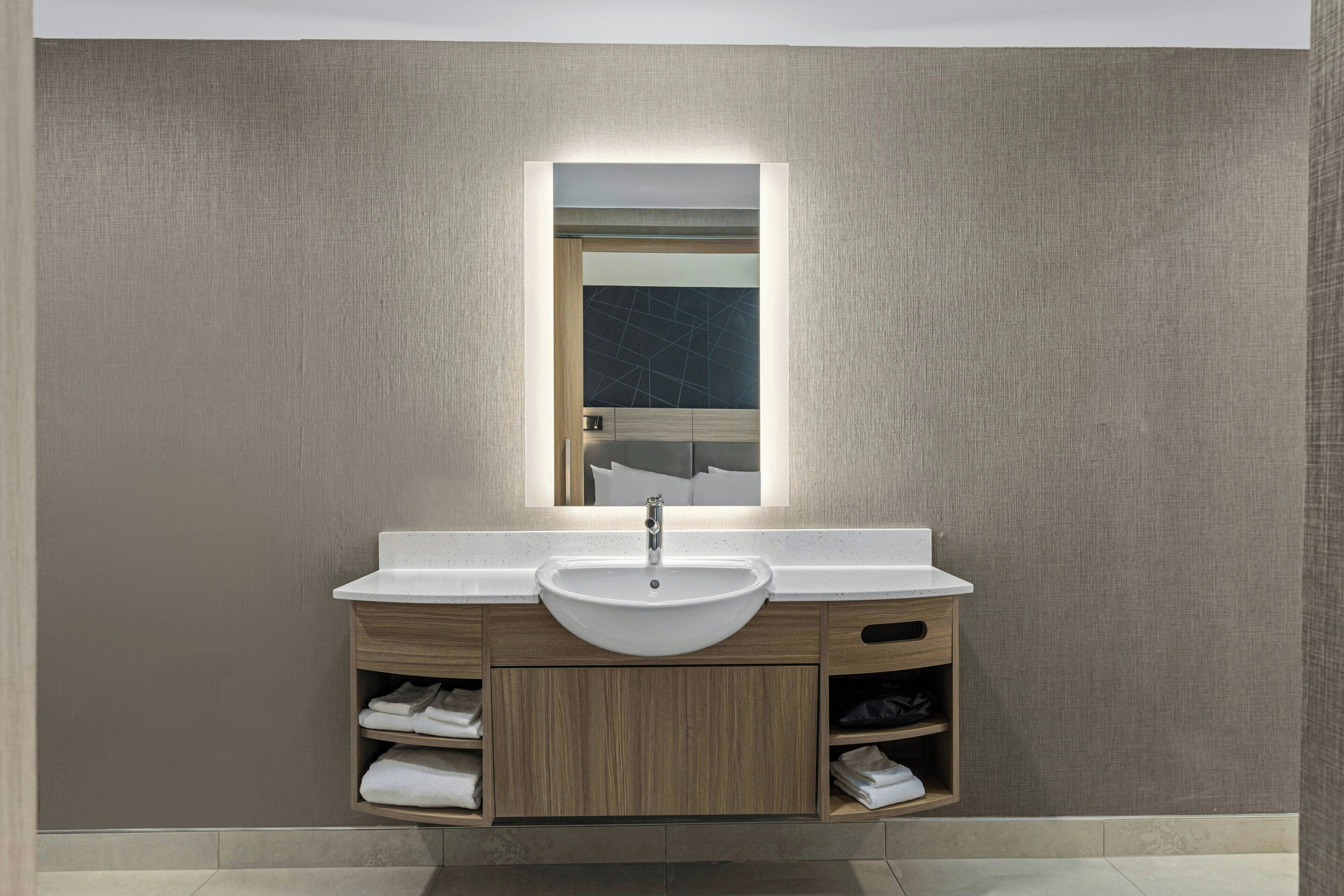 A modern bathroom with a white sink, wooden vanity, and a mirror with built-in lighting.