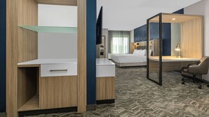 A hotel room with a bed, a desk, a chair, a mirror, and a TV.