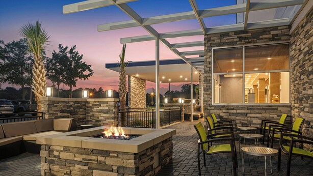 An outdoor patio area with a fire pit, seating, and a covered section with a view of the interior.