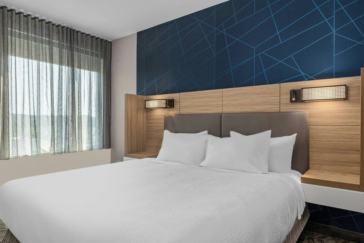 A modern hotel room with a large bed, wooden headboard, and a geometric-patterned wall.