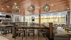 A spacious dining area with wooden tables and chairs, a central seating area with a sofa, and large windows providing natural light.