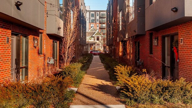 A narrow alleyway between two modern buildings with brick facades, a clear sky, and a red car parked in the distance. - Perfect getaway in Corktown! (Detroit)