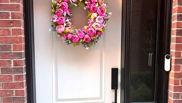 En vit dörr med en hjärtformad blomsterkrans, en svart dörrklocka och en glasdörr med ett metallhandtag.