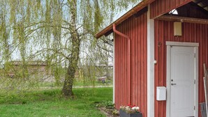 A red wooden building with a white door, a small garden area with flowers, and a tree with green leaves. - Pet friendly apartment in Kristianstad (Kristianstad)