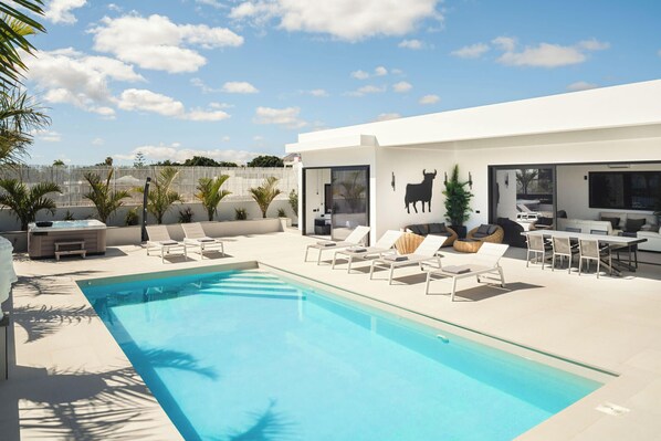 A modern outdoor pool area with lounge chairs, a hot tub, and a dining area with a large window overlooking the pool.