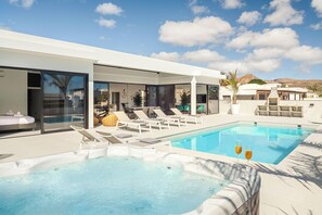 A modern pool area with lounge chairs, a hot tub, and a clear view of the surrounding landscape.