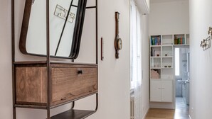 Un couloir avec une armoire en bois, un miroir, une horloge et une étagère blanche remplie de livres.