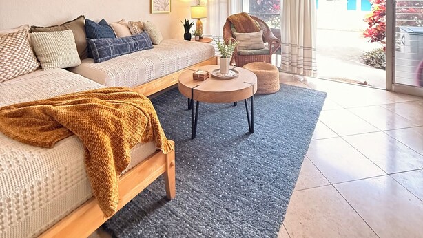 A modern living room with a sofa, a coffee table, a chair, and a large window. - Kaua Corner (Paia)