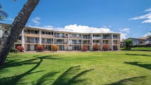 A multi-story hotel with a flat roof, balconies, and a well-maintained lawn. - Kaua Corner (Paia)