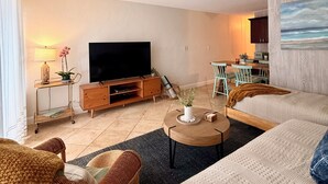 A well-lit living room with a flat-screen TV, wooden furniture, a ceiling fan, and a painting on the wall. - Kaua Corner (Paia)