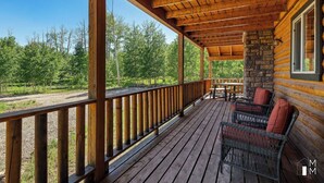 Une terrasse en bois, dotée de chaises en osier et d’un pilier en pierre, qui offre une vue sur une zone boisée.